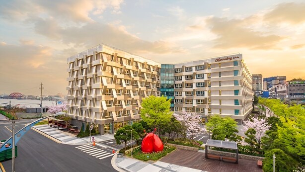 Een modern hotel met een unieke geometrische gevel, gelegen nabij een waterkant met kersenbloesems.