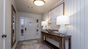 A hallway with a wooden bench, two wall-mounted lamps, a patterned rug, and a door with a stone accent. - Upscale Lake Retreat on Large Private Lot, Expansive Deck, Boat Dock & Hot Tub! (Hot Springs)
