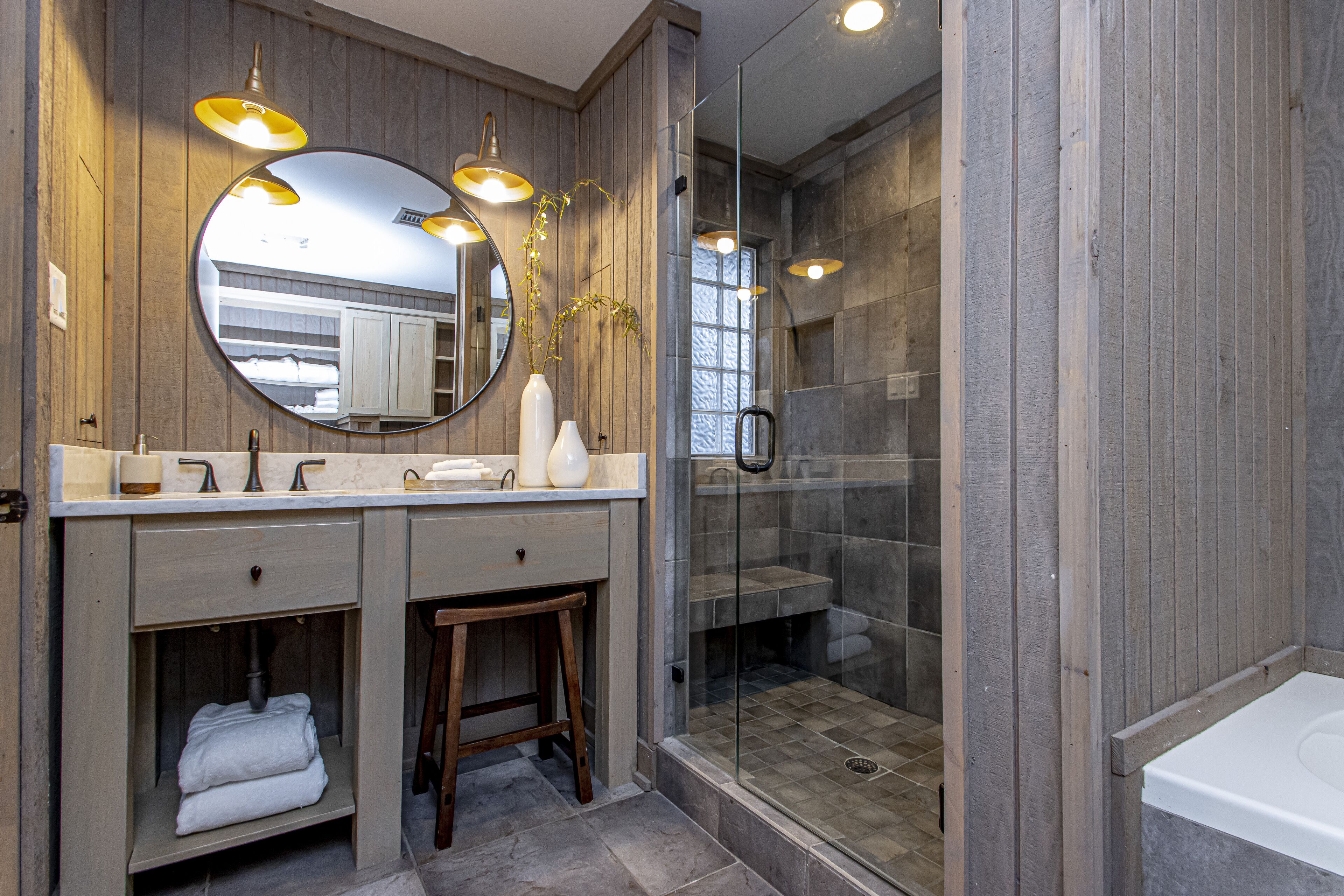 Un baño moderno con paneles de madera, un espejo grande, lavamanos dobles, una ducha con mampara de vidrio y una bañera.