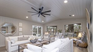 A spacious living room with a white color scheme, featuring a ceiling fan, large windows, and a cozy seating area with a sofa and chairs. - Upscale Lake Retreat on Large Private Lot, Expansive Deck, Boat Dock & Hot Tub! (Hot Springs)