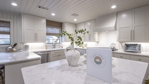 A modern kitchen with white cabinetry, a marble countertop, and a vase with green plants. - Upscale Lake Retreat on Large Private Lot, Expansive Deck, Boat Dock & Hot Tub! (Hot Springs)