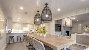 A spacious kitchen with a long wooden table, white wicker chairs, and pendant lights. - Upscale Lake Retreat on Large Private Lot, Expansive Deck, Boat Dock & Hot Tub! (Hot Springs)