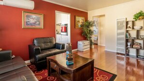 A living room with a red wall, a black leather sofa, a wooden coffee table, and a red carpet. There is a kitchen visible through an open doorway. - Luxury stay near Santana Row for vacation/business (San Jose)