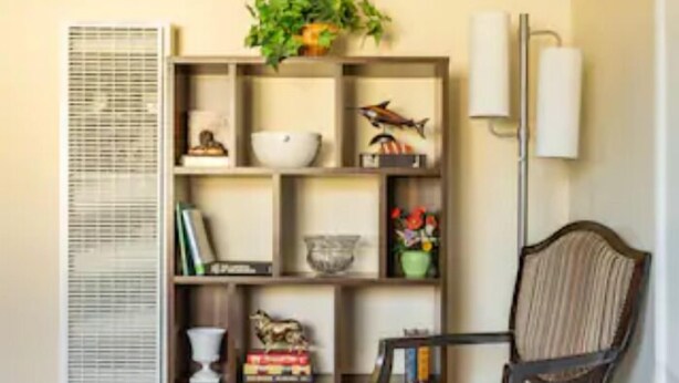 A room with a wooden floor, a bookshelf with various decorative items, a chair, and a floor lamp. - Luxury stay near Santana Row for vacation/business (San Jose)