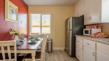 A compact kitchen with a dining table, chairs, a refrigerator, a microwave, and cabinets.