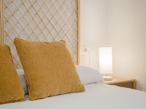 Habitación de hotel con cama, dos almohadas, mesita de noche con lámpara y cabecero decorado con un diseño.