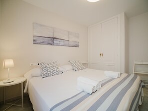 Hotellihuone, jossa on suuri sänky, kaksi tyynyä, yöpöytä lampun kanssa ja taulu seinällä.