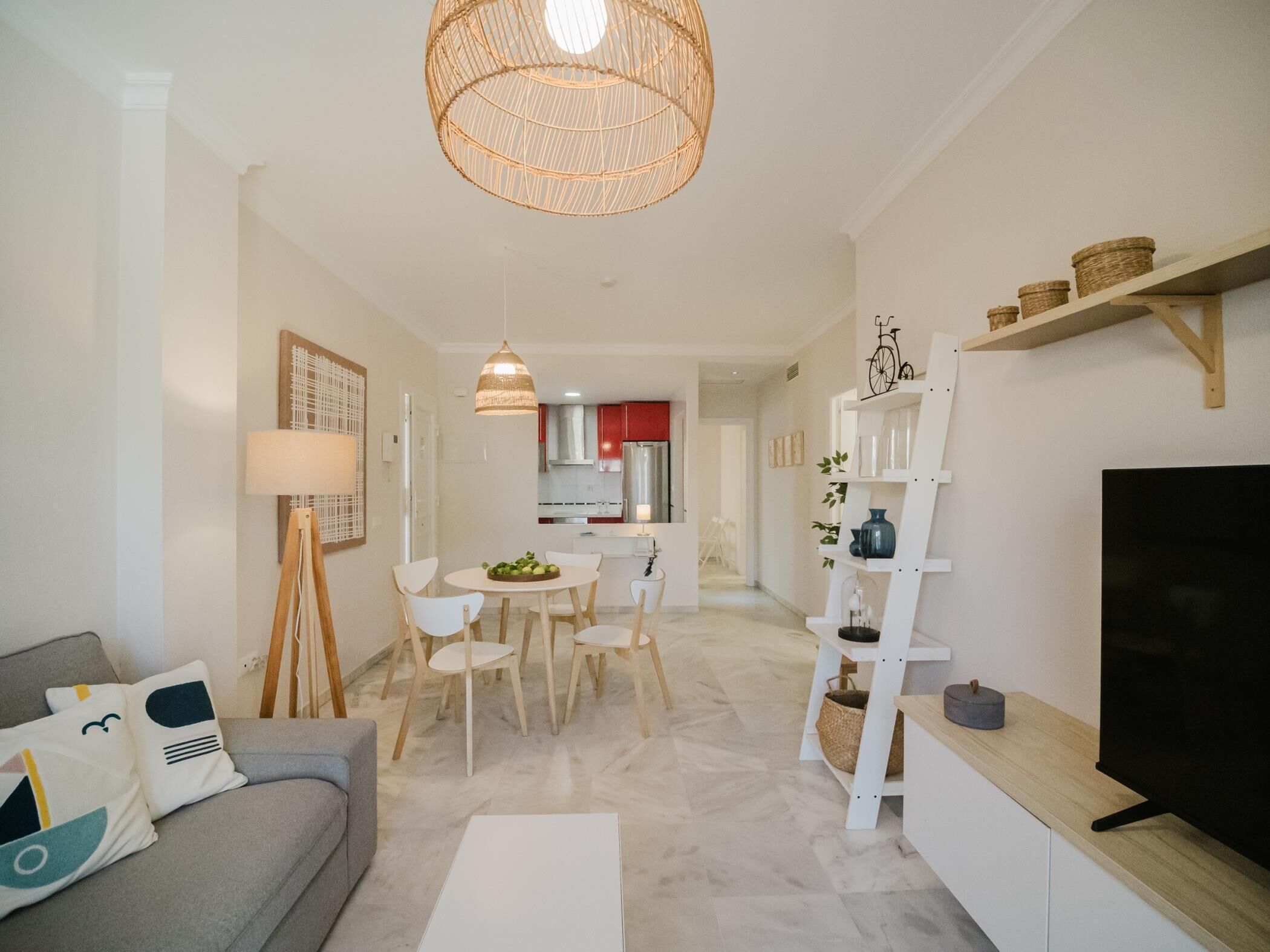 Ein modernes Wohnzimmer mit einer Couch, einem Esstisch mit Stühlen, einem Fernseher und einer Küche im Hintergrund.