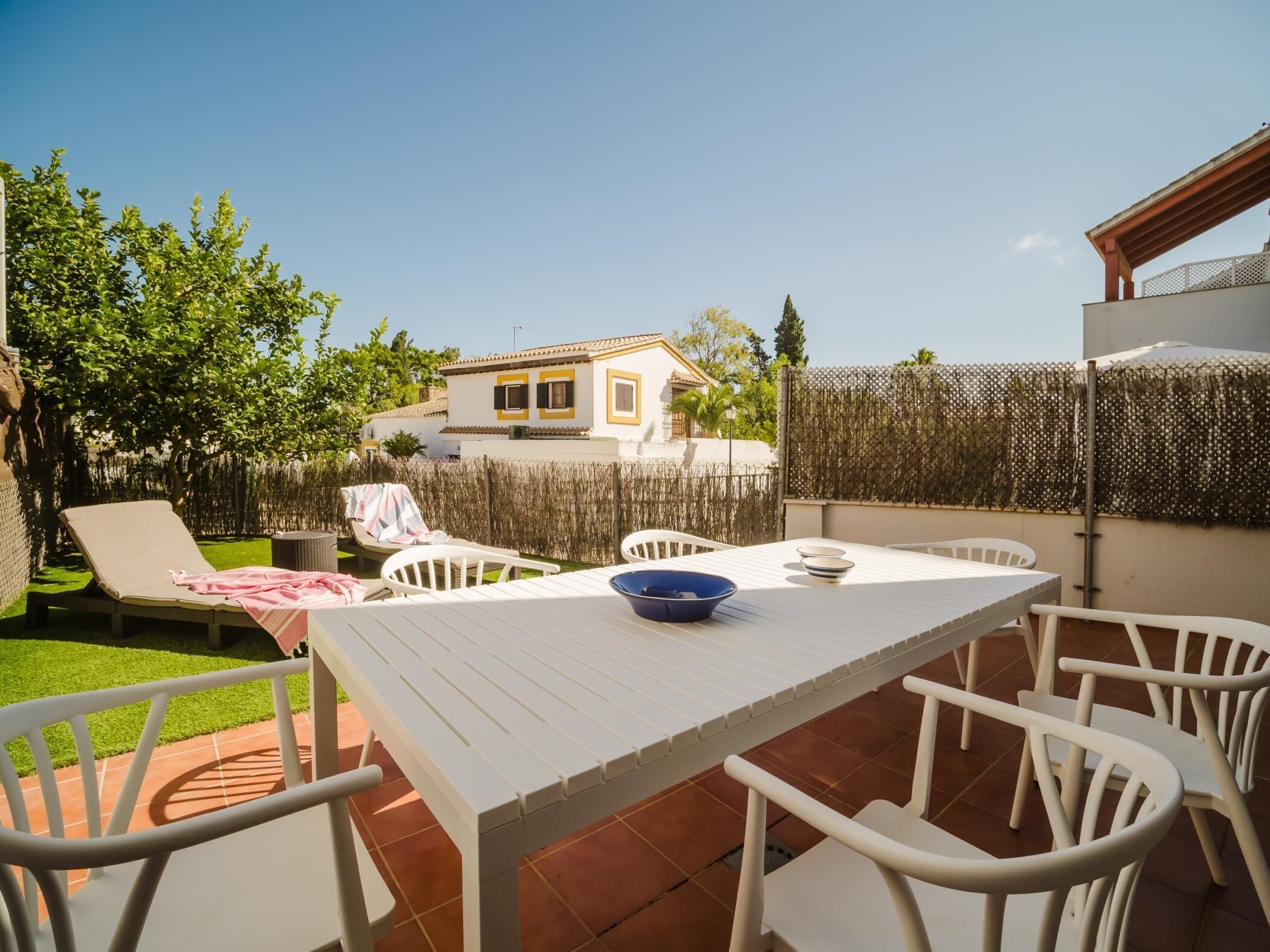 An outdoor patio with a white table and chairs, a blue bowl, and a covered seating area with a pink towel.