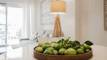 A wooden bowl of limes on a table in a bright room with a lamp and a sofa in the background.