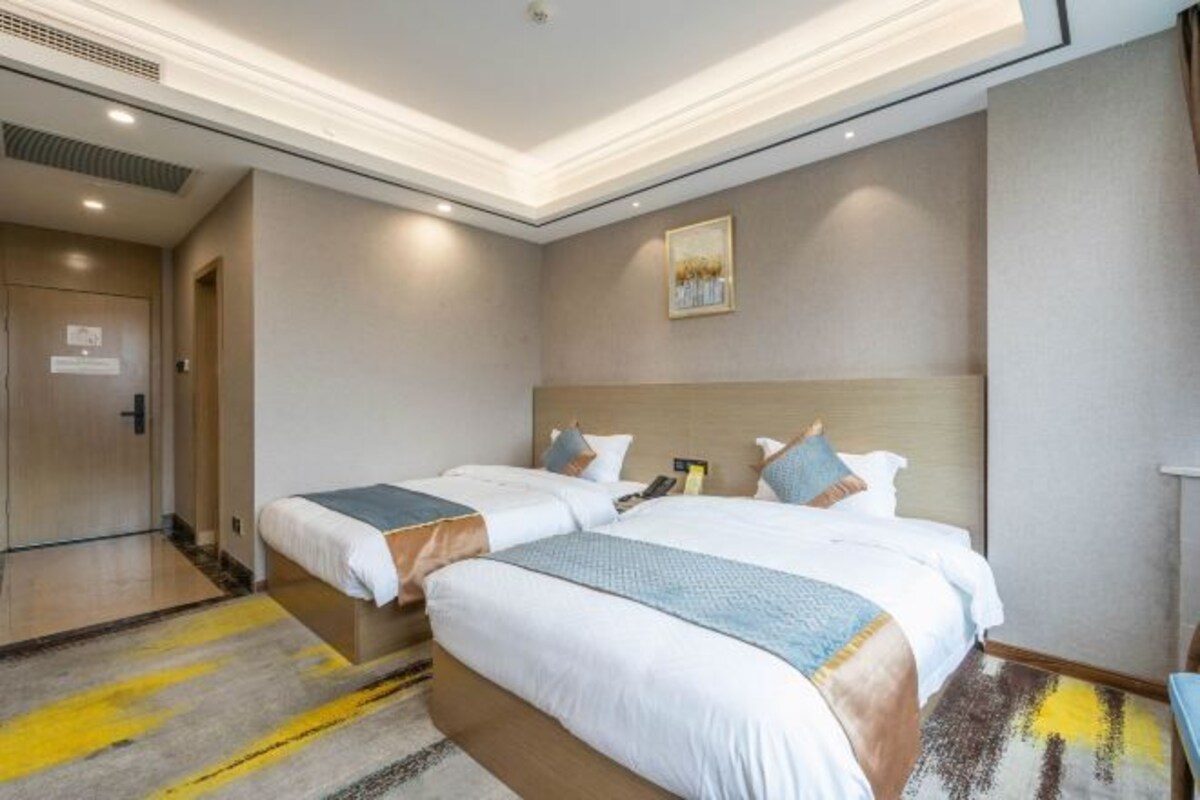 A hotel room with two beds, a wooden headboard, a painting on the wall, and a small table with a phone.