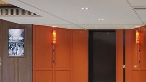 Un hall d’hôtel moderne avec un grand ascenseur, des panneaux de bois et une affiche encadrée représentant une vue panoramique de la ville.