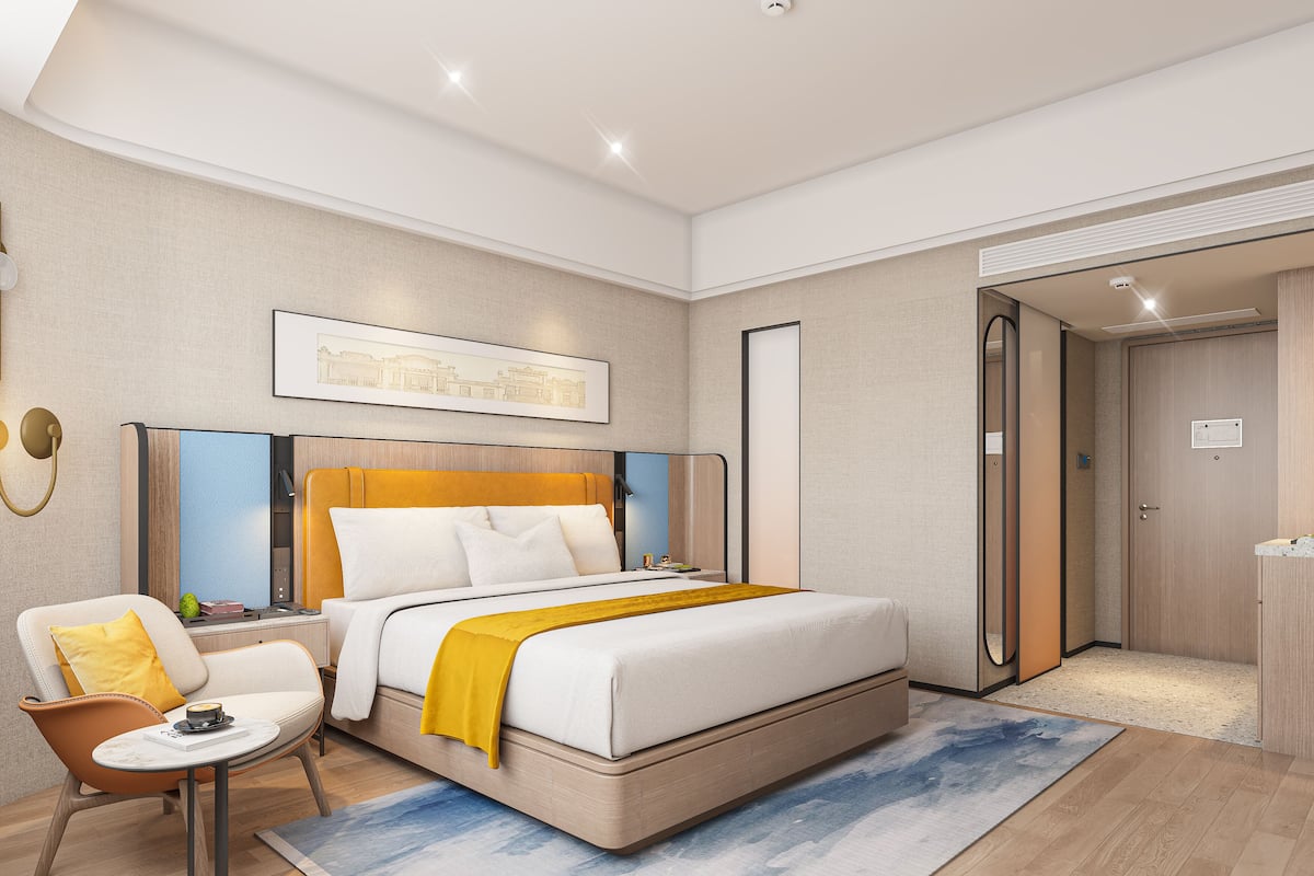 Moderni hotellihuone, jossa on sänky, tuoli, pieni pöytä ja ovi.
