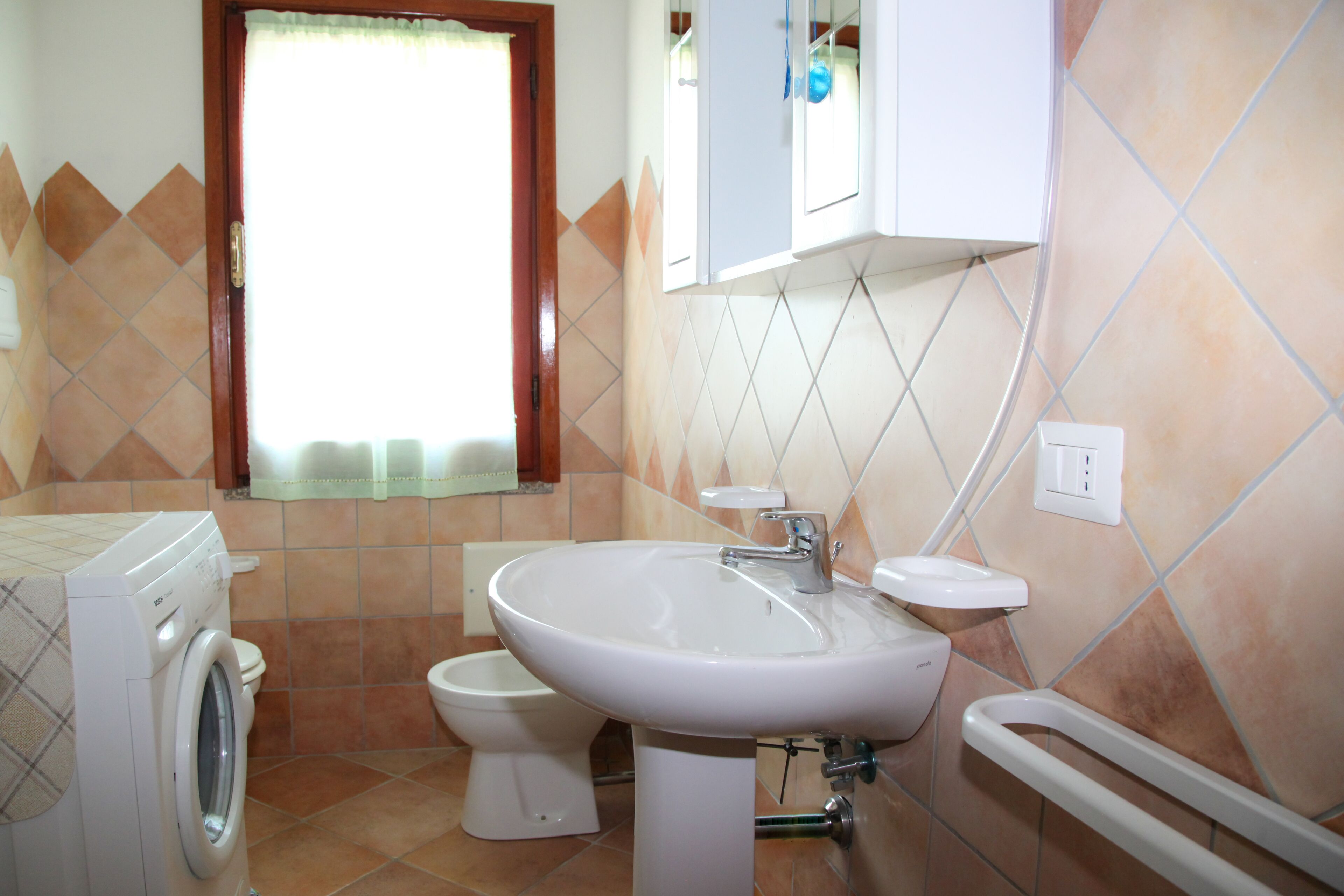 Une salle de bain équipée d’un lave-linge, de toilettes, d’un lavabo et d’une fenêtre avec des rideaux.