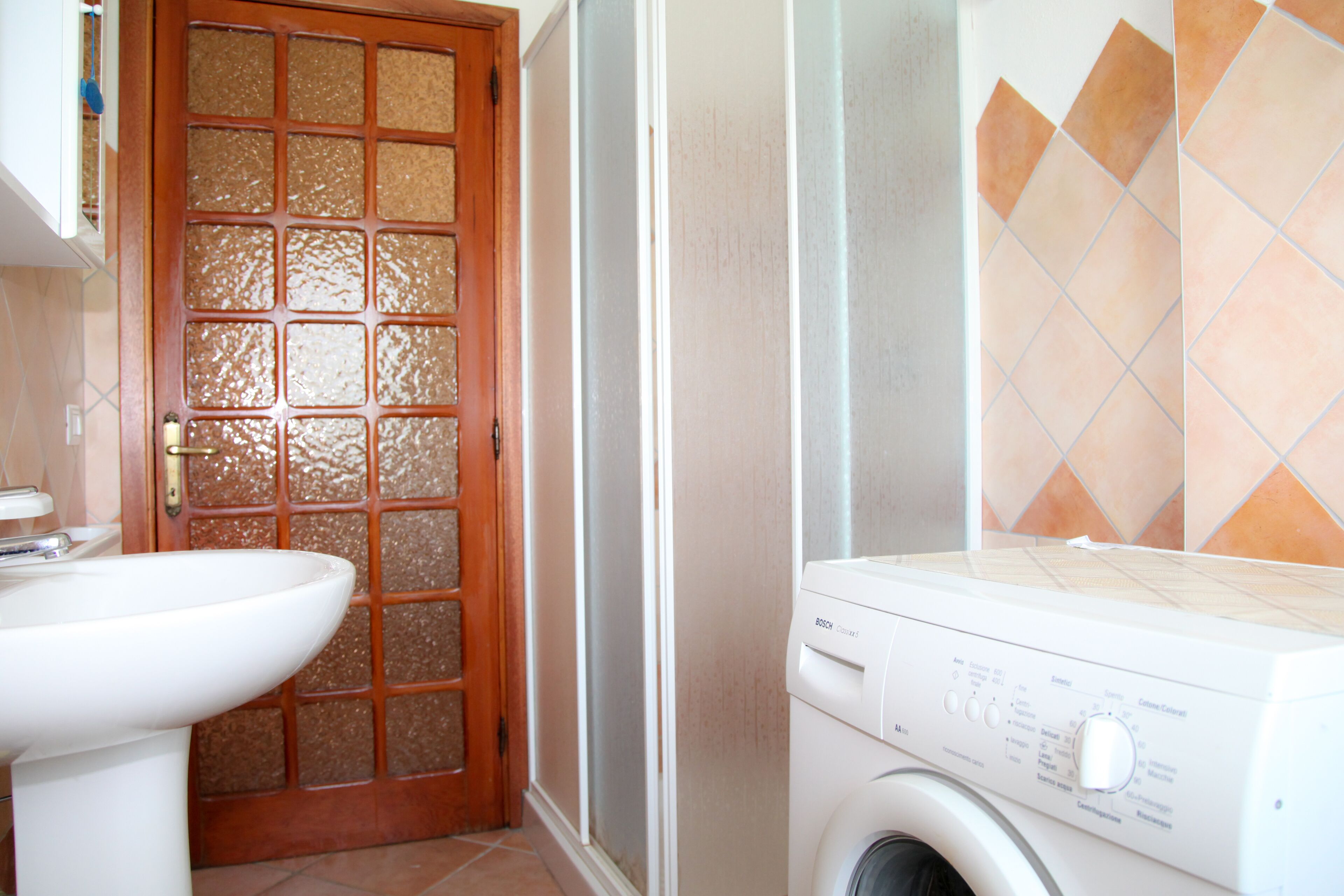 Une salle de bain avec un lavabo blanc, une porte en bois dotée de panneaux de verre et un lave-linge.