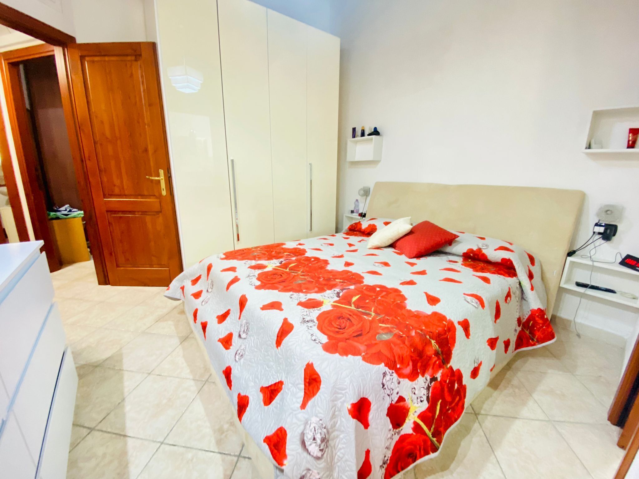 A bedroom with a bed, a wardrobe, a nightstand, and a wall-mounted shelf.