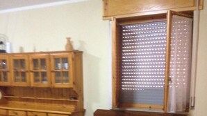 A dining area with a table covered in a sunflower-patterned tablecloth, wooden benches, and a window with blinds. - Bosamarina House (Bosa)