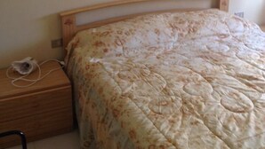 A bedroom with a wooden bed frame, a floral bedspread, a small bedside table with a lamp, and a wall-mounted picture. - Bosamarina House (Bosa)