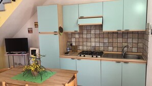 A compact kitchen with light blue cabinets, a wooden dining table with chairs, a stove, and a sink. - Appartamento Le Querce 4 (San Teodoro)