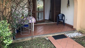 A covered patio area with a table and chairs, a potted plant, and a door leading to an interior space. - Appartamento Le Querce 4 (San Teodoro)