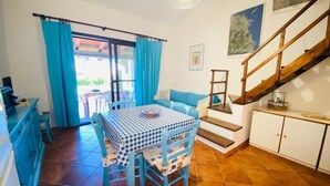 A cozy room with a checkered table, blue chairs, a sofa, and a staircase. - Appartamento Cala d'Ambra (San Teodoro)