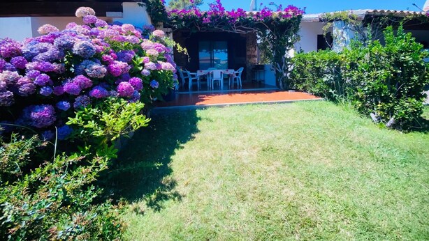 A patio area with outdoor seating, surrounded by lush greenery and flowering plants. - Appartamento Cala d'Ambra (San Teodoro)