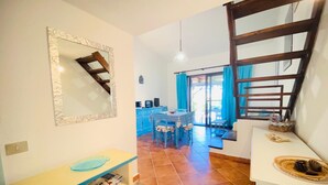 A compact living space with a kitchen area, a dining table, and a staircase. - Appartamento Cala d'Ambra (San Teodoro)