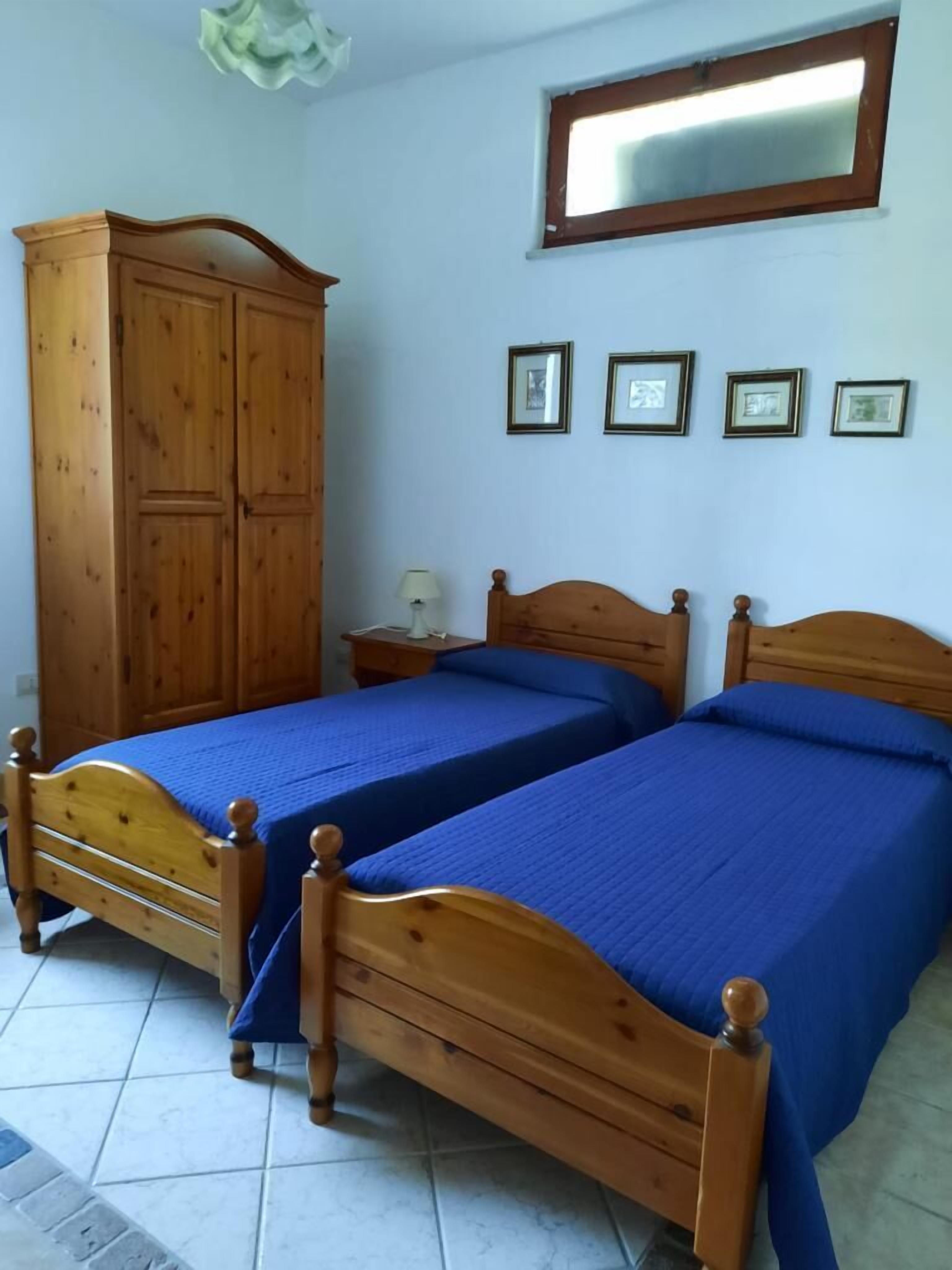 A bedroom with two wooden beds, a wardrobe, a nightstand, and a mirror on the wall.