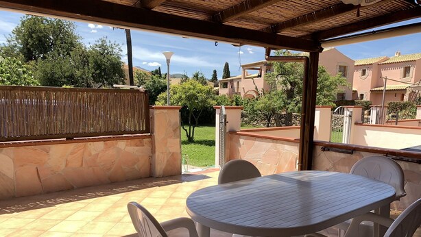 A covered patio with a round table and four chairs, surrounded by stone walls and a bamboo fence.