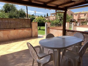 A covered patio with a round table and four chairs, surrounded by stone walls and a bamboo fence. - Appartamento I Gerani 3 San Teodoro Centro (San Teodoro)