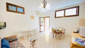 Una sala de estar con sofá, una mesa de centro de vidrio, un comedor con mesa y sillas, y una cocina con microondas.