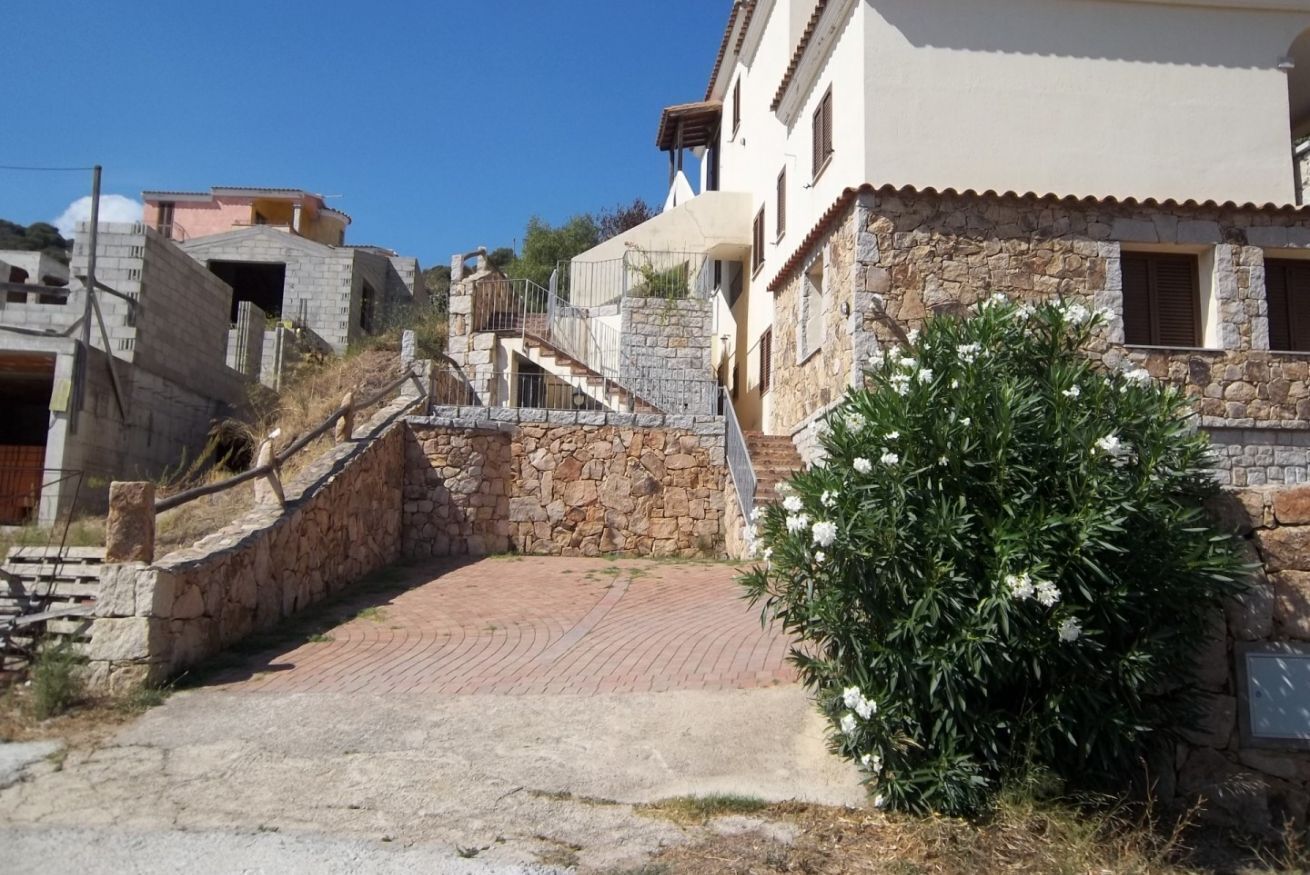Una scala in pietra conduce a un edificio con facciata in pietra e un piccolo giardino con fiori bianchi.