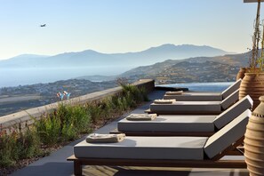 A terrace with lounge chairs and a view of the coastline and mountains.