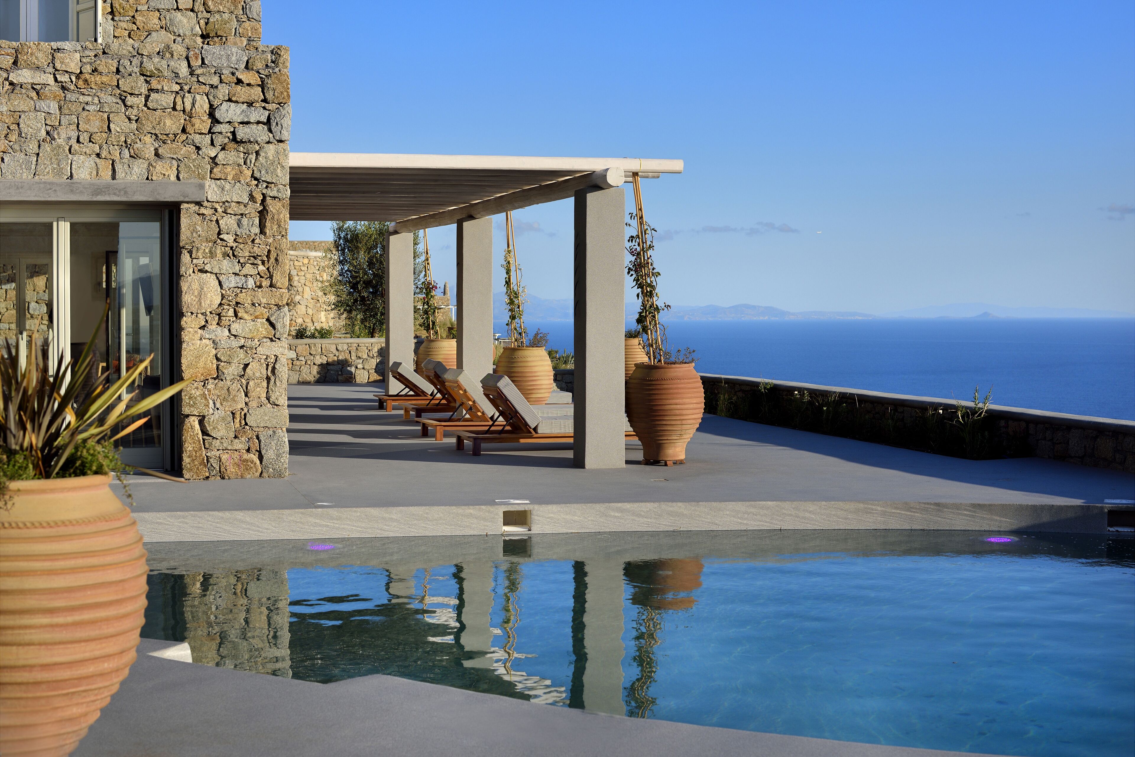A pool area with a stone building, lounge chairs, and large planters.