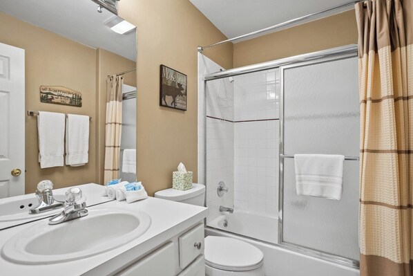 A bathroom with a shower, toilet, sink, and towel racks.