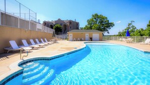Une piscine avec des chaises longues, un petit bâtiment et une clôture.