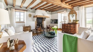 A spacious living room with exposed wooden beams, a fireplace, comfortable seating, and a large window. - Ferme Labourdine avec piscine 5 étoiles - Sare (Sare)