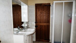Un baño con puerta de madera, lavamanos blanco y cabina de ducha de vidrio.