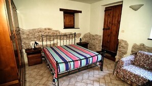 Un dormitorio con cama, mesita de noche, cómoda, sofá y paredes de piedra.