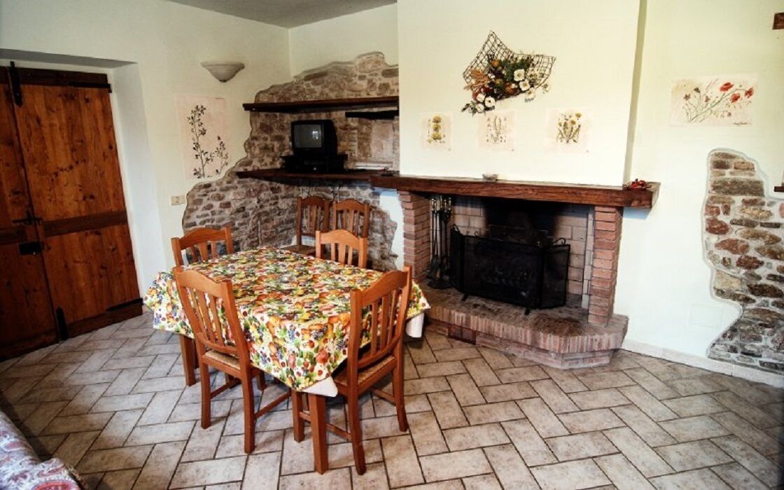 Un comedor con chimenea de piedra, sillas de madera y una mesa cubierta con mantel floreado.