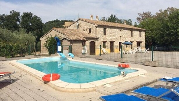 Zona de piscina con un edificio de piedra, sillas de descanso y un flotador.