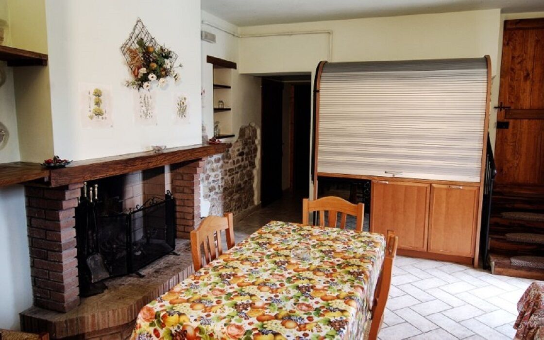 Un comedor con chimenea de ladrillo, una mesa cubierta con mantel floreado y un mueble de madera.