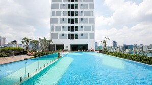 En modern byggnad med en pool på taket, omgiven av grönska och med stadens silhuett som bakgrund.