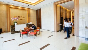 En hotellobby med en receptionsdisk, en sittgrupp med röda stolar och en trappa som leder till ett annat våningsplan.