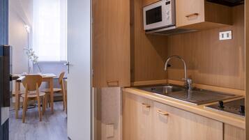 Una cocina compacta con microondas integrado, lavamanos de acero inoxidable y armarios de madera.