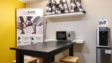 A kitchenette with a microwave, a water dispenser, and a refrigerator. There is a 'BAR' sign above the counter and a promotional poster on the wall.