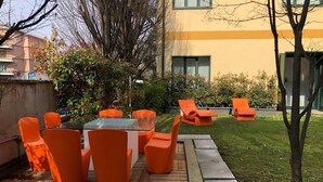 An outdoor seating area with orange chairs and a glass-top table, surrounded by a well-maintained lawn and a building in the background. - Residence Cimarosa (Milan)