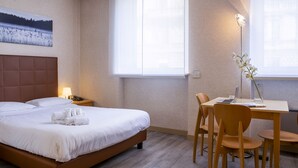 A hotel room with a bed, bedside table, lamp, and a desk with chairs. - Residence Cimarosa (Milan)