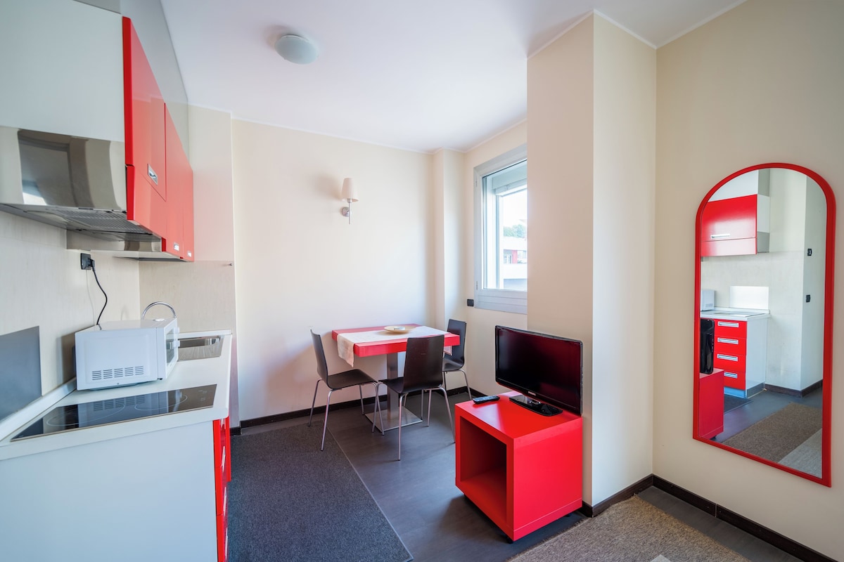 A compact room with a kitchenette, a dining area, a television, and a mirror.