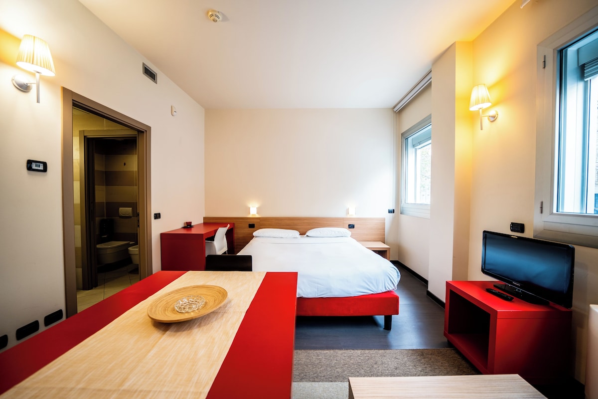 A hotel room with a bed, a TV, a desk, and a bathroom.